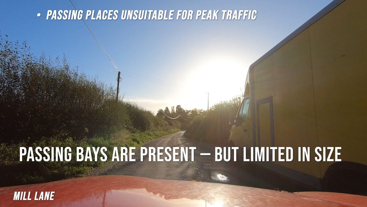 Driver's-eye view of Mill Lane at low sun: a large yellow box van squeezing past, illustrating how little width the lane offers.