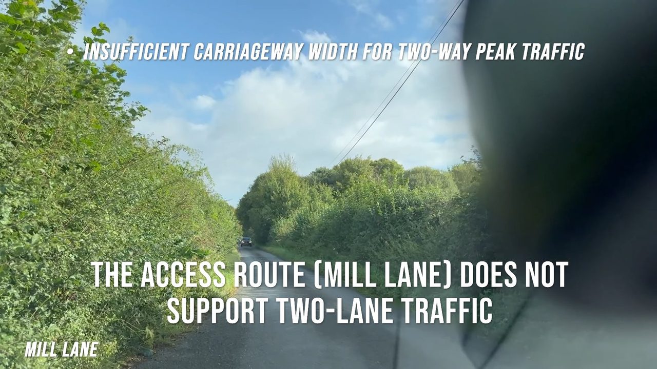 Mill Lane: a narrow single-track lane between high hedgerows with an oncoming car ahead, viewed through a vehicle windscreen.
